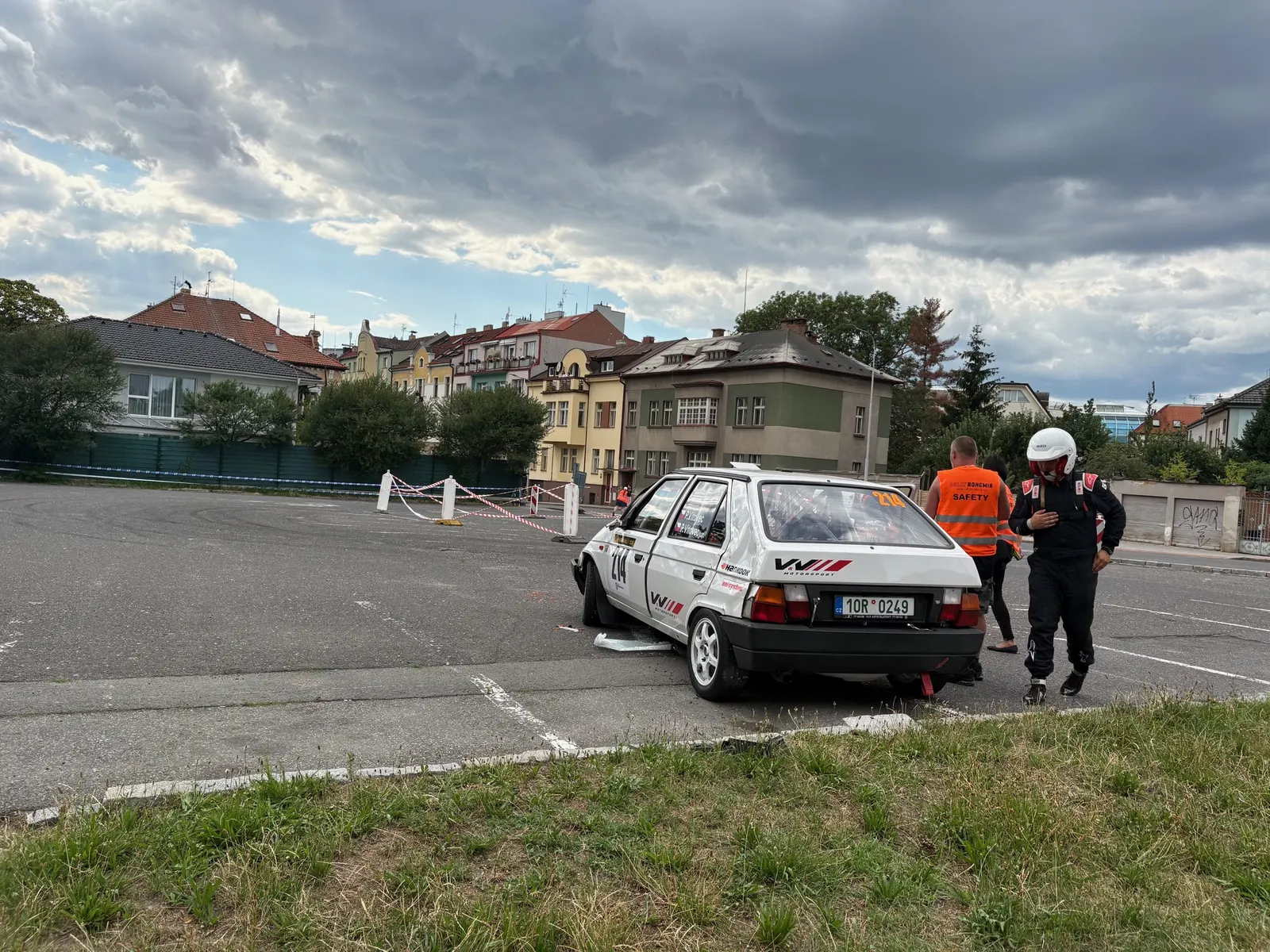 Škoda Favorit #214 v livreji VW Motorsport po havárii, pilot ve žlutočervené kombinéze a bílé přilbě, marshall v oranžové safety vestě