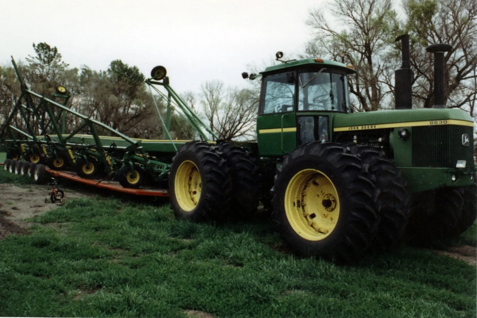 Zelený John Deere 8630 s dvojmontáží kol a nářadím