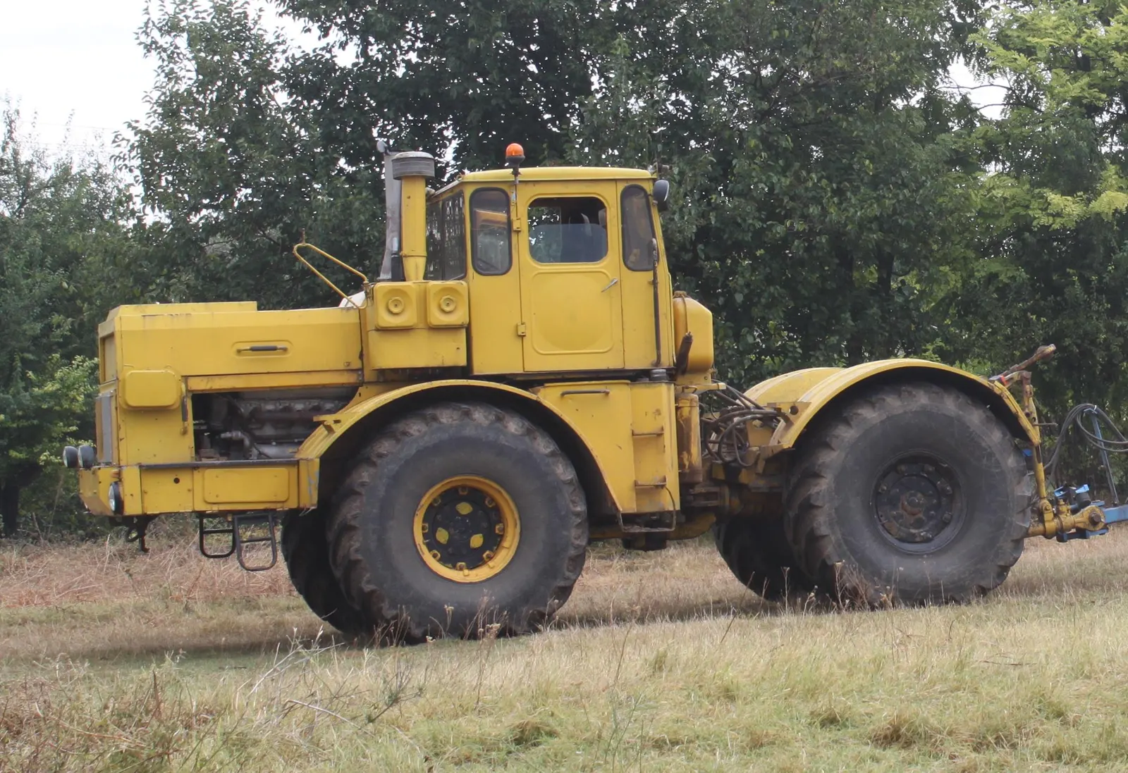Žlutý K-701 stojící v trávě u stromů