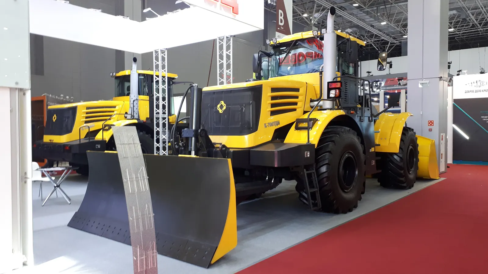 Žlutý K-708UDM s radlicí ve výstavní hale