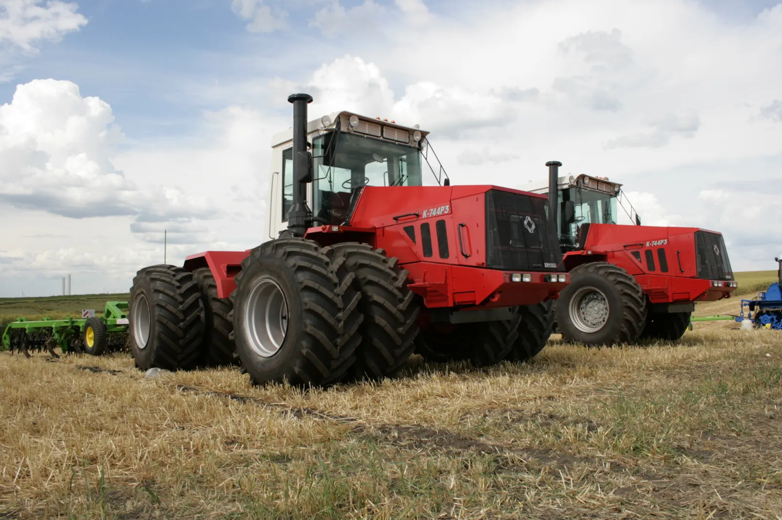 Dva červené Kirovce K-744R3 s dvojmontáží kol na strništi
