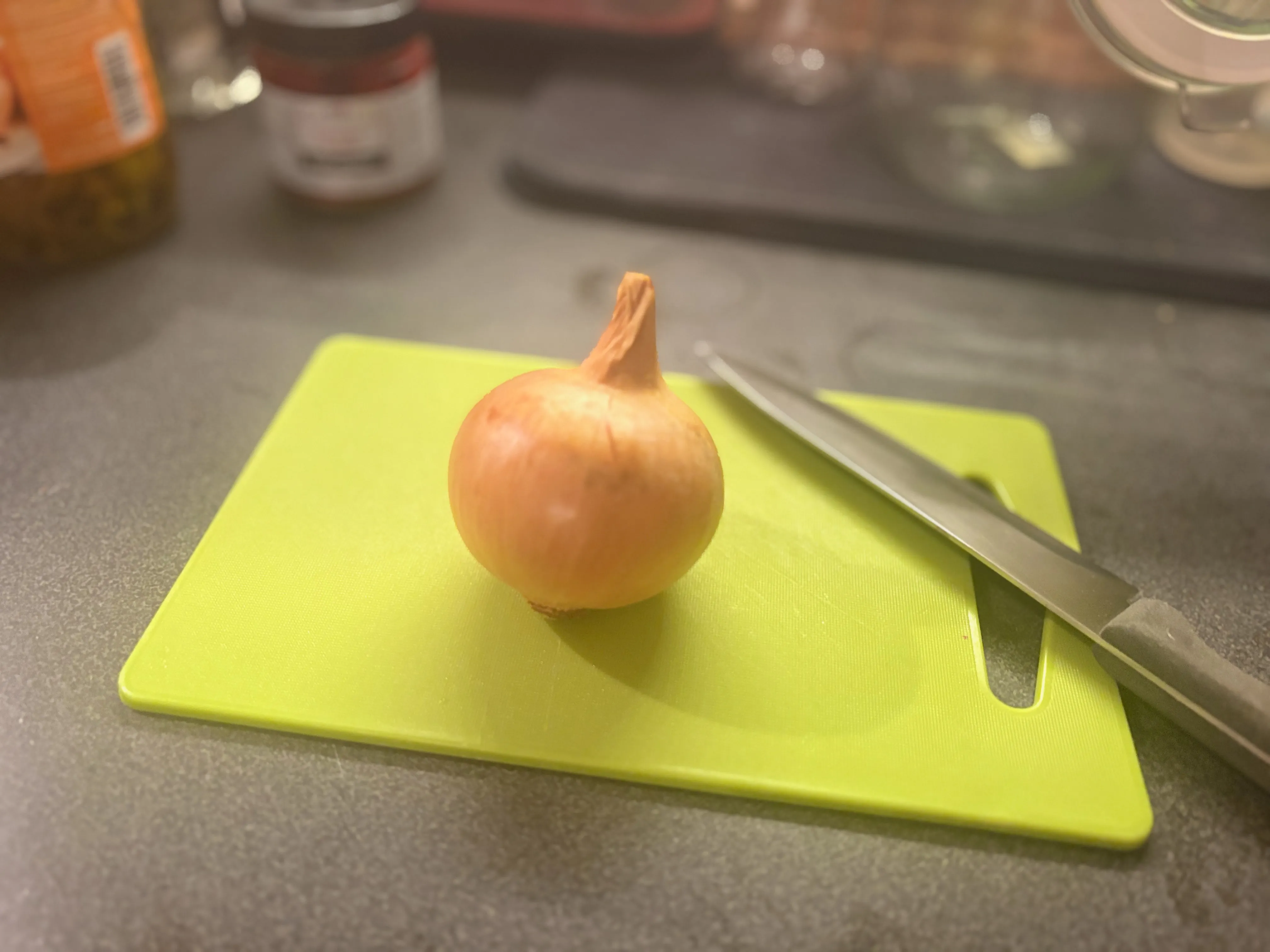 Celá cibule na zeleném plastovém prkénku vedle kuchyňského nože