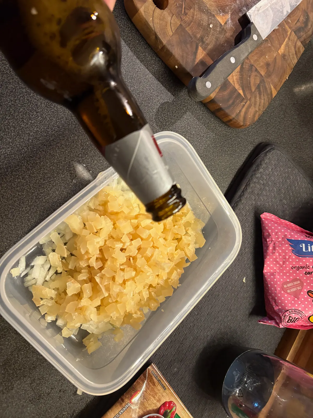Kostičky sýra a nakrájená cibule v plastové misce, do které se lije pivo z lahve