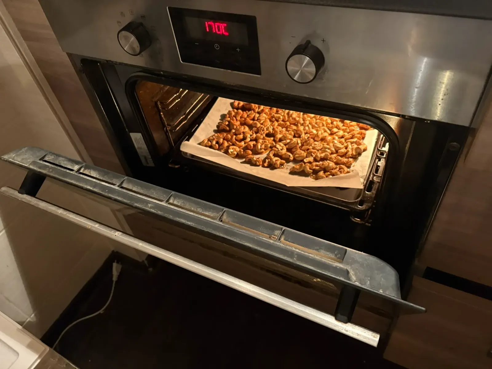 Otevřená trouba, na plechu dozlatova pečené kešu, na displeji 170 °C