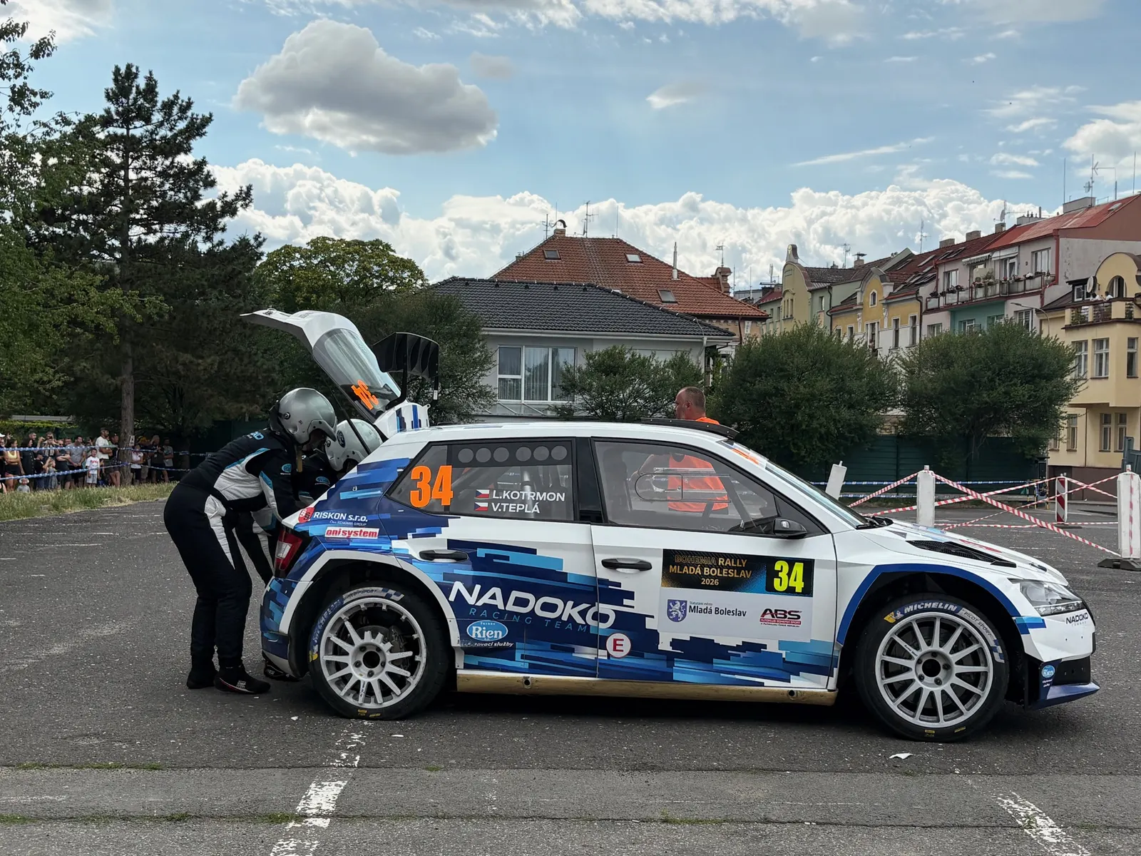 Škoda Fabia Rally2 v Nadoko Racing livreji v servisní zóně, spolujezdec u otevřeného kufru s rezervním kolem