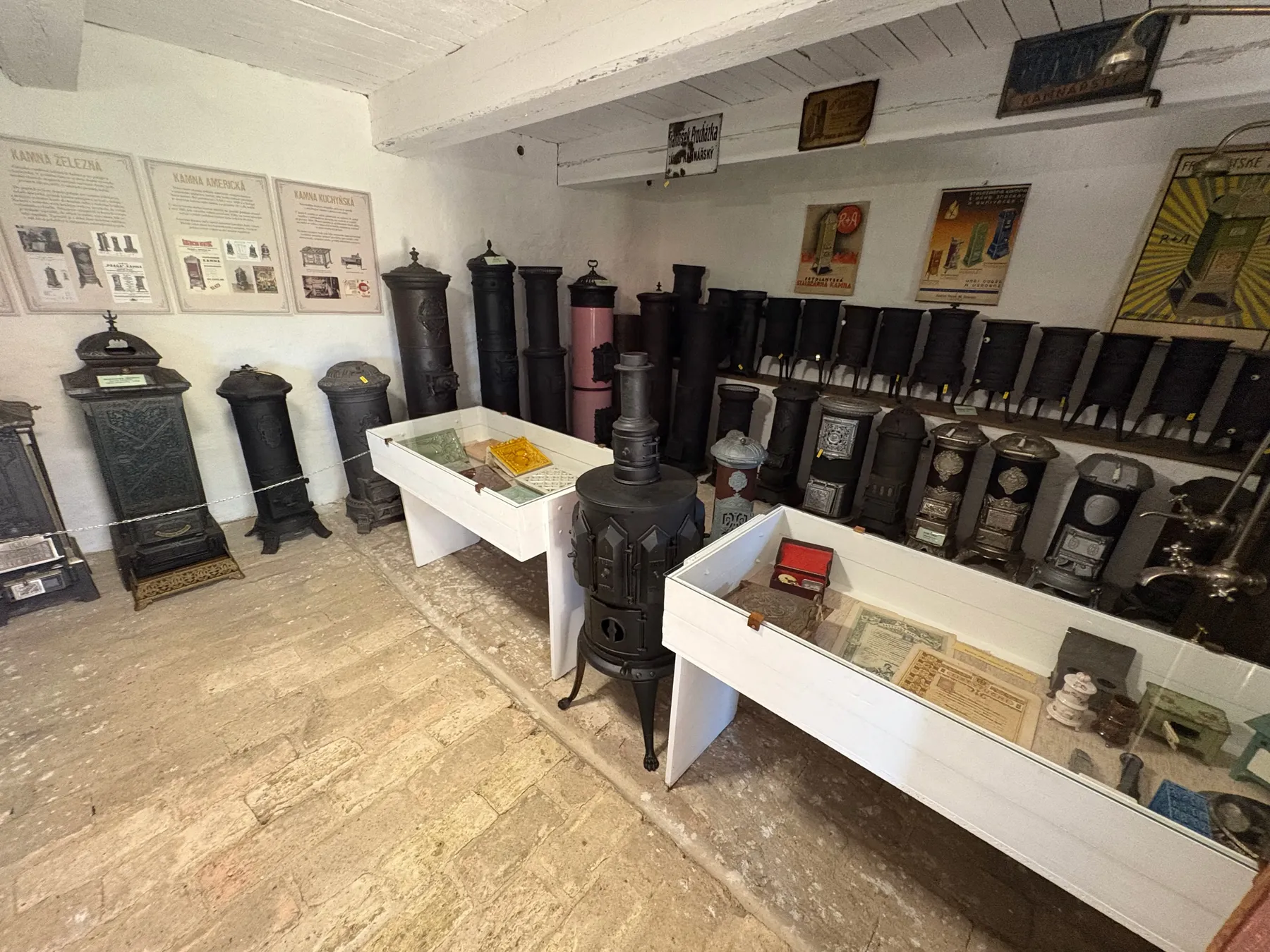 Další pohled na expozici kamen - řada litinových kamen na bílých podstavcích