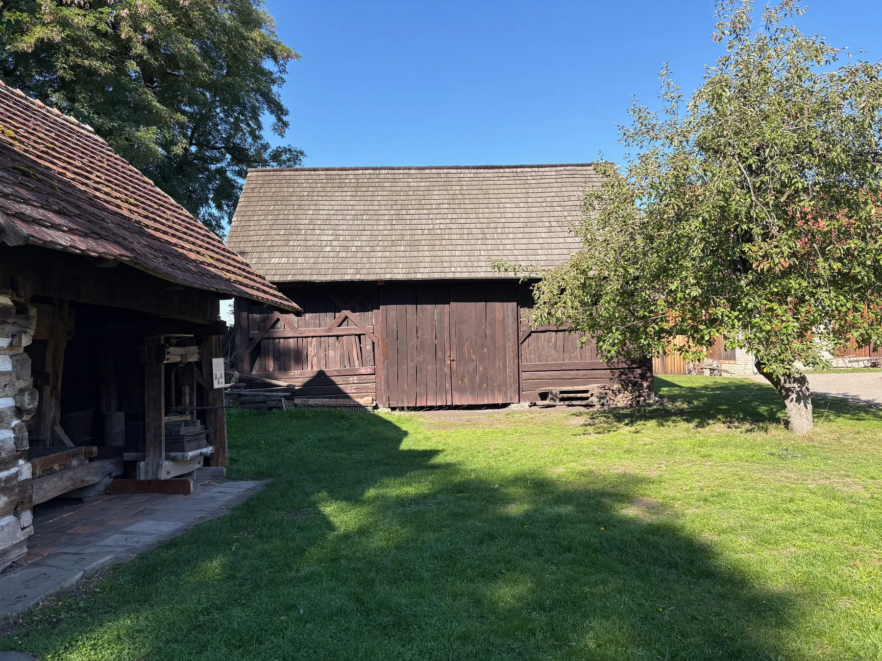 Boční pohled na dřevěnou stodolu s roubenou spodní částí a bedněnou horní částí, tašková střecha
