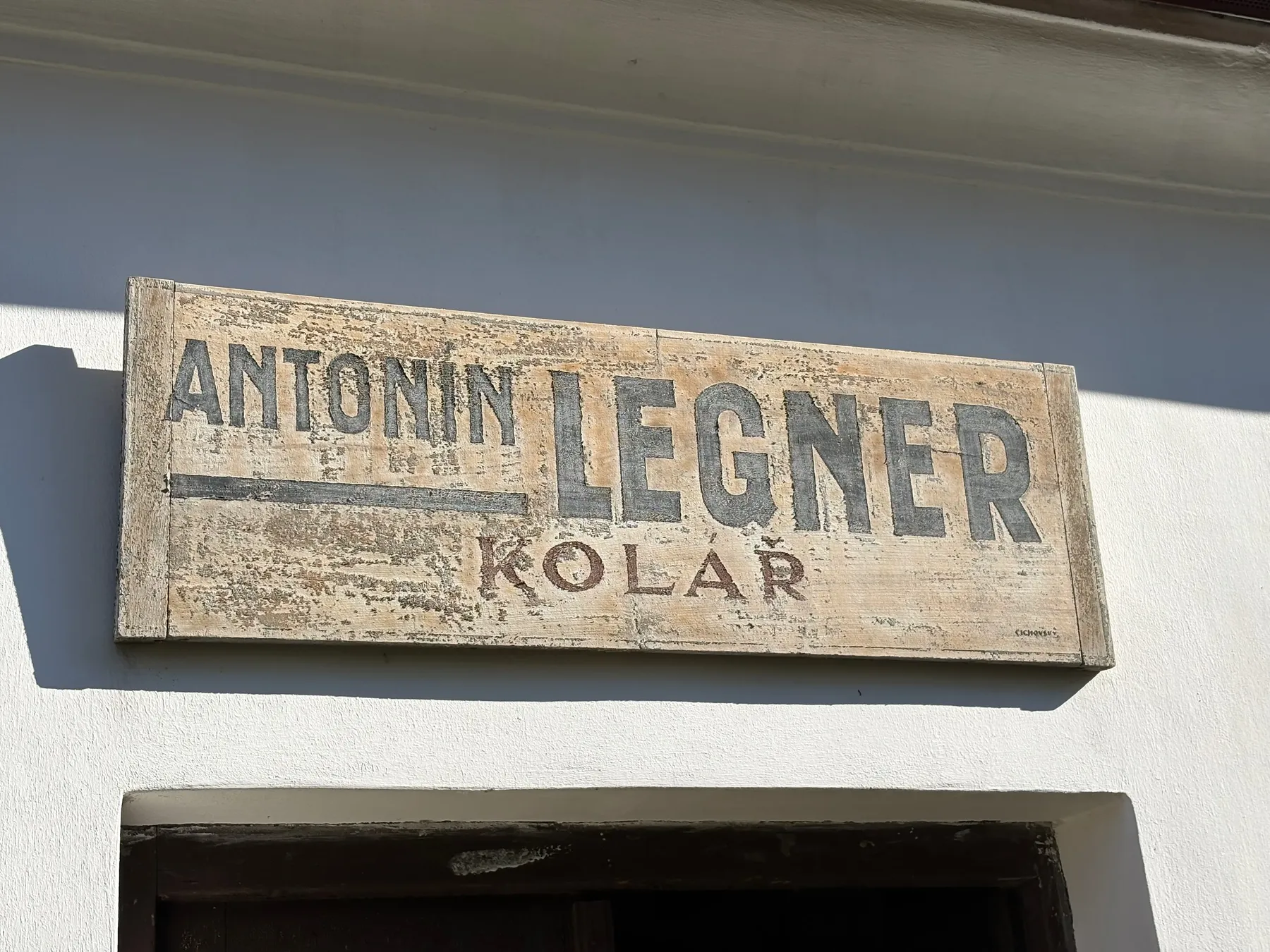 Dřevěná firemní cedule s nápisem ANTONÍN LEGNER KOLAŘ na omítnuté zdi