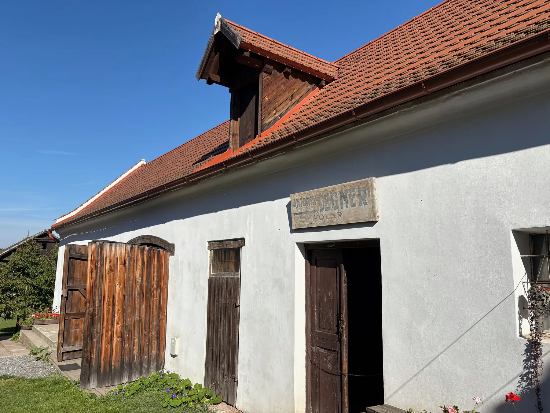 Bílá stavba s červenou taškovou střechou, dřevěné dveře a vrata