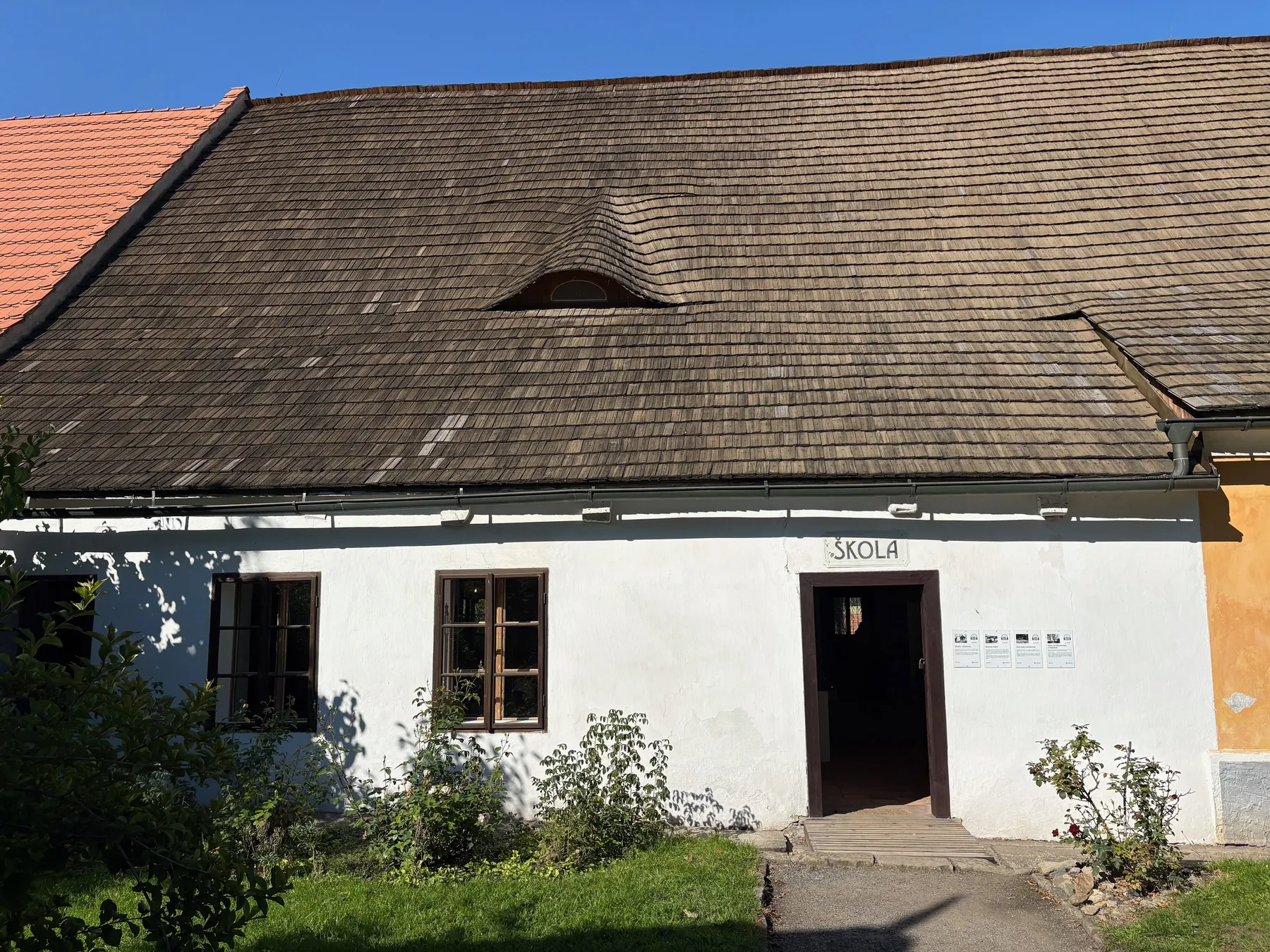 Bílá jednopodlažní stavba s cihlovou střechou a nápisem ŠKOLA nad vchodem