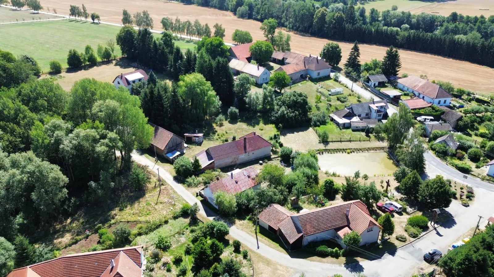 Štěpánov u Leštiny z výšky - pole, náves s rybníčkem, roztroušená vesnice mezi lesy