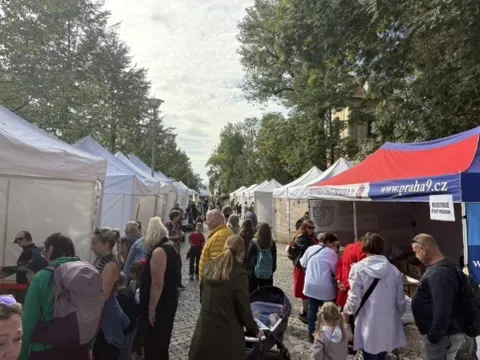 Alej stánků s bílými plachtami, lidé procházejí