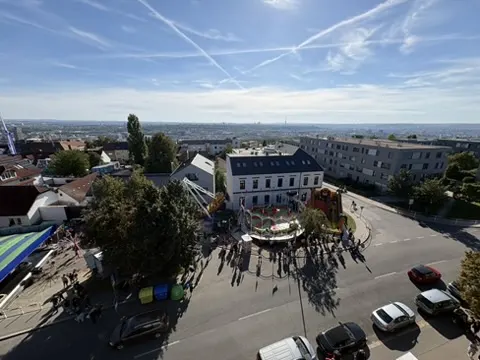 Pohled z ruského kola na Prosek - řetěz atrakcí, žluto-zelená střecha stánků a v pozadí panorama Prahy